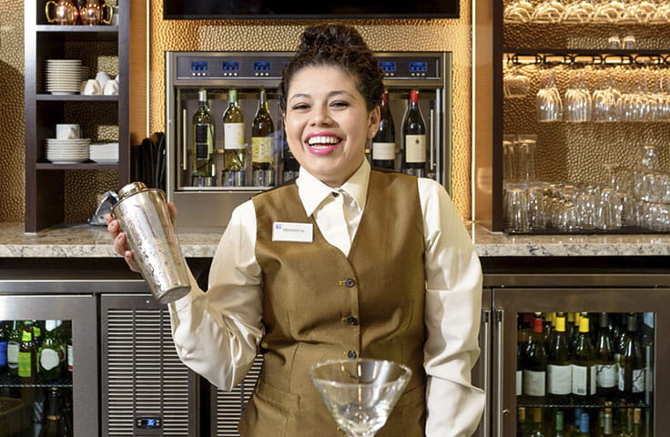 Woman bartender making a drink behind bar.